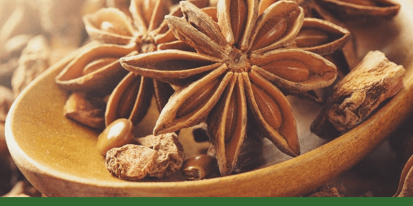 Whole star anise pods in a wooden spoon.