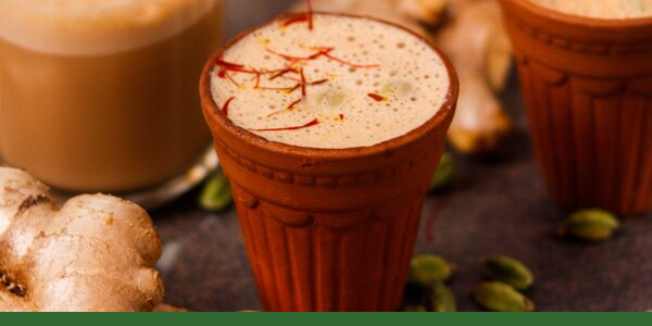 Clay cups of cardamom tea with green cardamom pods and ginger