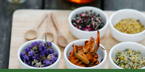 Bowls of dried herbs beside a glass teapot, ready for blending herbal tea at home