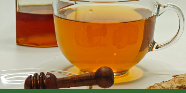 Glass cup of ginger tea with honey, a honey dipper and fresh ginger