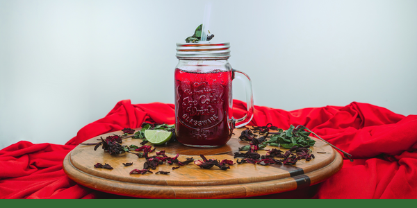 Red hibiscus tea in a mason jar with lime and dried hibiscus, with a Gaia Garden green line along the bottom