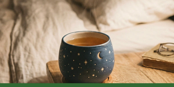 A warm cup of herbal tea beside cream bedding and a book.